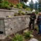 Landscape contractor inspecting a retaining wall on a sloped residential property in British Columbia.